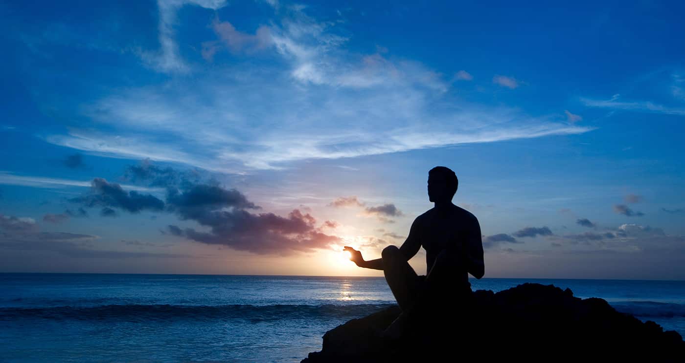 Meditating man captures the distant sun at a beach